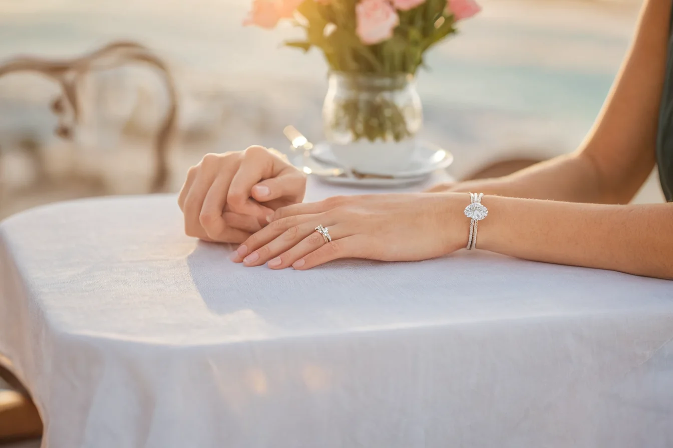 Couple's hands clasped together wearing diamond ring and bracelet at seaside table